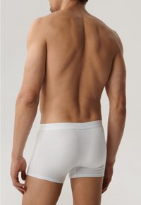 Białe bokserki wykonane z miękkiego materiału, z gładką gumką w pasie i dopasowanym krojem, pokazane na męskim modelu z tyłu.