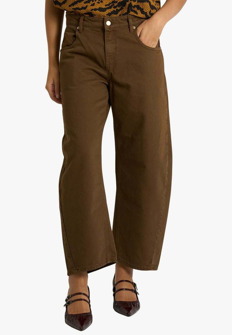 Pantaloni marroni a gamba larga in cotone dal design pulito, con tasche frontali e vita alta. Abbinati a scarpe nere con cinturini.