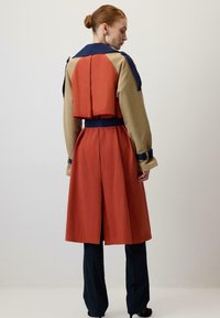 Trench coat a bloques de color en naranja, beige y marino. Incluye una parte trasera acampanada y puños abotonados. Tejido suave con un diseño estructurado.