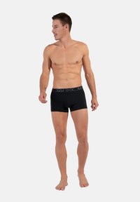 Pantaloni boxer neri con una cintura elastica che presenta il nome del marchio. Design aderente e tessuto morbido, con una texture liscia.