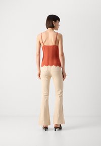 Débardeur tricoté texturé de couleur rouille avec un ourlet à volants et des bretelles ajustables, associé à un pantalon évasé beige clair et des mules noires à talons.