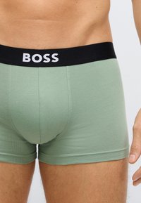 Zielone bawełniane bokserki z czarną elastyczną talią, na której znajduje się napis "BOSS" w białych literach. Gładka tekstura i dopasowany krój.