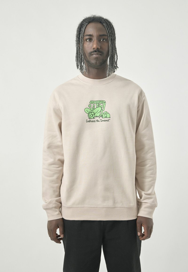 Light beige sweatshirt made of soft fabric. Features a green graphic design with text "Embrace the Timeout" on the front. This design includes playful elements.