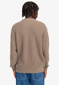 Bruine gebreide trui met ribbelstructuur, ronde hals en lange mouwen. Gekleed met blauwe jeans, die een relaxte pasvorm en casual ontwerp tonen.