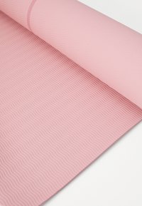 Saltea de yoga roșie rulată cu un model texturat undulat, din material sintetic, care prezintă o suprafață netedă pentru prindere și suport.