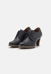 Zapatos de cuero negros con puntera redondeada, diseño de cordones y un tacón de madera de altura media. Textura suave y sutil detalle de costura.