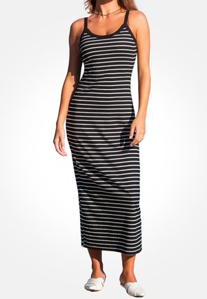 Robe maxi rayée noir et blanc à fines bretelles, silhouette ajustée, tissu doux et longueur à la cheville. Chaussures blanches simples à enfiler.