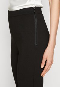 Schwarze hoch taillierte Leggings aus dehnbarem Material, mit einem seitlichen Reißverschluss für ein einfaches Anziehen. Glatte Textur mit einer eleganten Passform.