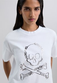 White cotton t-shirt featuring a silver graphic of a skull and crossbones with the word "SCALPERS" integrated into the design.