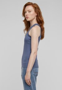 Ujjatlan bordázott tank top puha kék színben, testhezálló szabással és sima textúrával, magas derekú farmernadrággal párosítva.