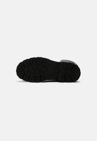 Suela de zapato de goma negra con un patrón de superficie profunda, que presenta púas triangulares para agarre y un borde plano en el talón. Acabado texturizado y resistente.