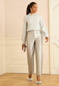 Ljusgrå stickad tröja med puffärmar och ett pärlbesatt halsband, i kombination med metalliska silverfärgade högmidjade byxor och skor med rosett. 