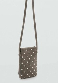 Torbica iz semiša v sivi barvi z belimi pikami čez ramo. Ima tanko zasnovo, nastavljiv trak in gladko teksturo.