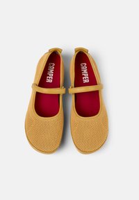 Zapatos Mary Jane de malla amarilla con puntera redondeada, plantillas rojas y una correa delgada sobre el empeine. La marca "Camper" es visible en el interior.