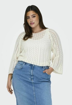 Pull en tricot crème avec un motif à mailles ouvertes, manches larges et col rond, assorti à une jupe en denim bleu clair.