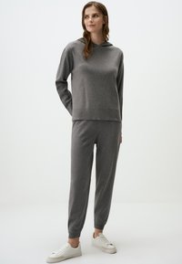 Grijze hoodie en bijpassende jogger set, gemaakt van zachte stof, met een ontspannen pasvorm, ribbels bij de manchetten en witte sneakers.