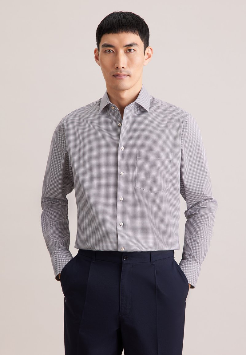 Camicia con bottoni a quadretti piccoli bianchi e blu navy, con colletto, maniche lunghe e taschino sul petto. Indossata con pantaloni blu navy.