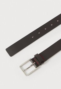 Σκούρα καφέ δερμάτινη ζώνη με ασημένια μεταλλική αγκράφα, κόκκινες ραφές και πολλαπλές τρύπες ρύθμισης κατά μήκος του ιμάντα.