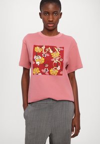 Rosa bomull t-skjorte med blomsterdesign i rødt, gult og hvitt, med korte ermer og en avslappet passform. Kombinert med gråstripete bukser.