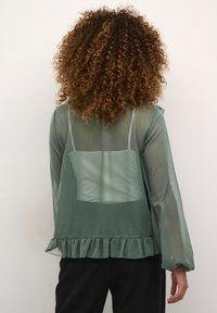 Blusa verde trasparente con maniche lunghe, orlo arricciato e dettaglio posteriore trasparente con uno strato interno aderente.