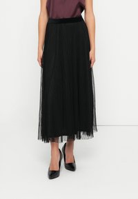 Black pleated tulle skirt with a soft texture, featuring a solid black waistband and a flowy, ankle-length design. Worn with black heels.