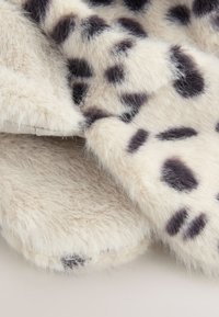 Imitace kožešiny v krémové barvě s černými skvrnami, měkká textura a huňatý vzhled, s našitým zatočeným okrajem a jemným leskem.
