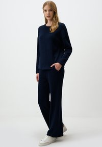 Navy knitted lounge set featuring a long-sleeve top with a crew neckline and wide-leg pants. Textured fabric with side pockets.