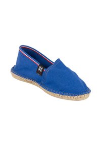 Chaussure slip-on en toile bleue avec une semelle en jute, présentant un accent rouge et blanc au niveau du col et des bords cousus pour plus de durabilité.