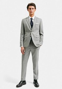 Ljusgrå kostym med slim fit, två knappar och slagkrage. Vit skjorta, mörk slips och svarta finskor kompletterar looken.