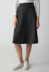 Gonna grigia a campana con una texture liscia, lunga fino al ginocchio e con una vita aderente, abbinata a sneakers bianche. Design semplice e funzionale.