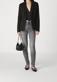 Blazer negro ajustado, top corto negro, jeans skinny grises, bolso negro con cadena y bailarinas negras con detalle de hebilla.