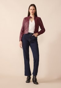 Burgunderfarget lærjakke med korte ermer og stående krage, kombinert med høytlivede mørke denimjeans og svarte ankelstøvler med spenner.