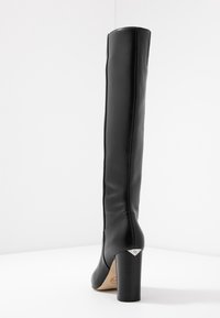 Vysoká černá kožená boty na podpatku s blokovým podpatkem na jednoduchém bílém pozadí, pohled ze zadu.