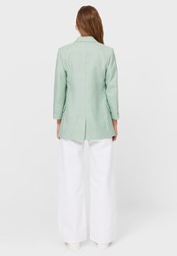 Blazer à carreaux vert clair avec un dos fendu et des manches trois-quarts, associé à un pantalon large blanc et des chaussures légères.
