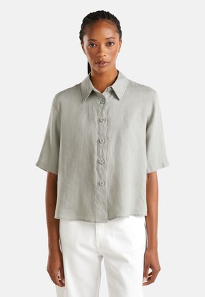 Lichtgrijs shirt met korte mouwen en een kraag, vijf knopen aan de voorkant en een iets cropped zoom. Glad textuur.