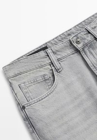 Jean en denim gris avec une finition texturée subtile. Comprend une poche avant, une fermeture par bouton, et une étiquette noire près de la ceinture.