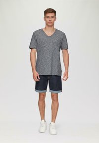 Szary t-shirt z dekoltem w kształcie litery V i krótkimi rękawami, zestawiony z ciemnoniebieskimi szortami dżinsowymi z podwiniętymi mankietami. Model nosi białe trampki. Prosta, swobodna stylizacja.