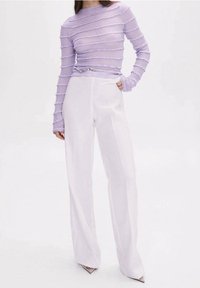 Femme portant un haut texturé à manches longues lavande rentré dans un pantalon blanc taille haute à jambes larges, avec des chaussures à bouts pointus.