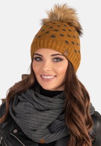 Knitted mustard beanie with black polka dots and a fur pom-pom on top. Paired with a gray ribbed scarf.