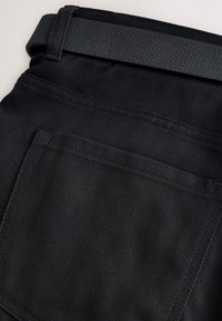 Gros plan sur la poche arrière d'un pantalon noir avec une ceinture noire texturée passée dans la boucle de ceinture.