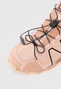 Ténis rosa claro com parte superior em malha respirável, apresentando atacadores e detalhes pretos, sola de borracha e um design texturizado.