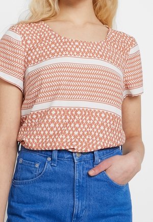 Camiseta de manga corta en melocotón con patrones y rayas geométricas blancas, hecha de tejido ligero, combinada con jeans de mezclilla azul de talle alto.