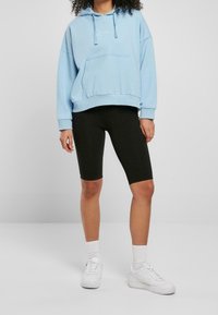 Ljusblå hoodie med framficka och dragsko, parat med svarta cykelbyxor och vita sneakers. Har ribbade manschetter och nederkant.