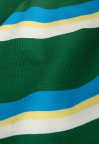 Tissu vert avec des rayures horizontales bleues, jaunes et blanches, montrant une texture tricotée et des plis subtils.