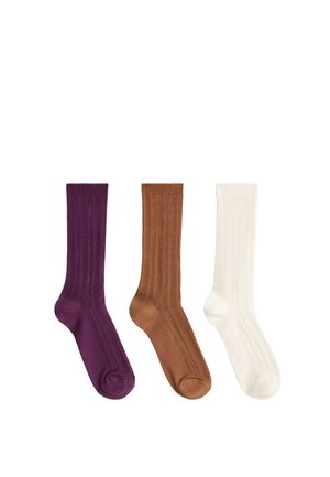 Trois paires de chaussettes en maille côtelée violet, marron et blanc, disposées côte à côte sur un fond blanc.