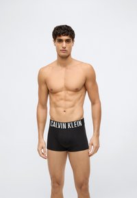 Svarta boxershorts med en Calvin Klein-logotyp på midjebandet. Materialet verkar vara slätt och åtsittande, vilket visar en minimalistisk design.