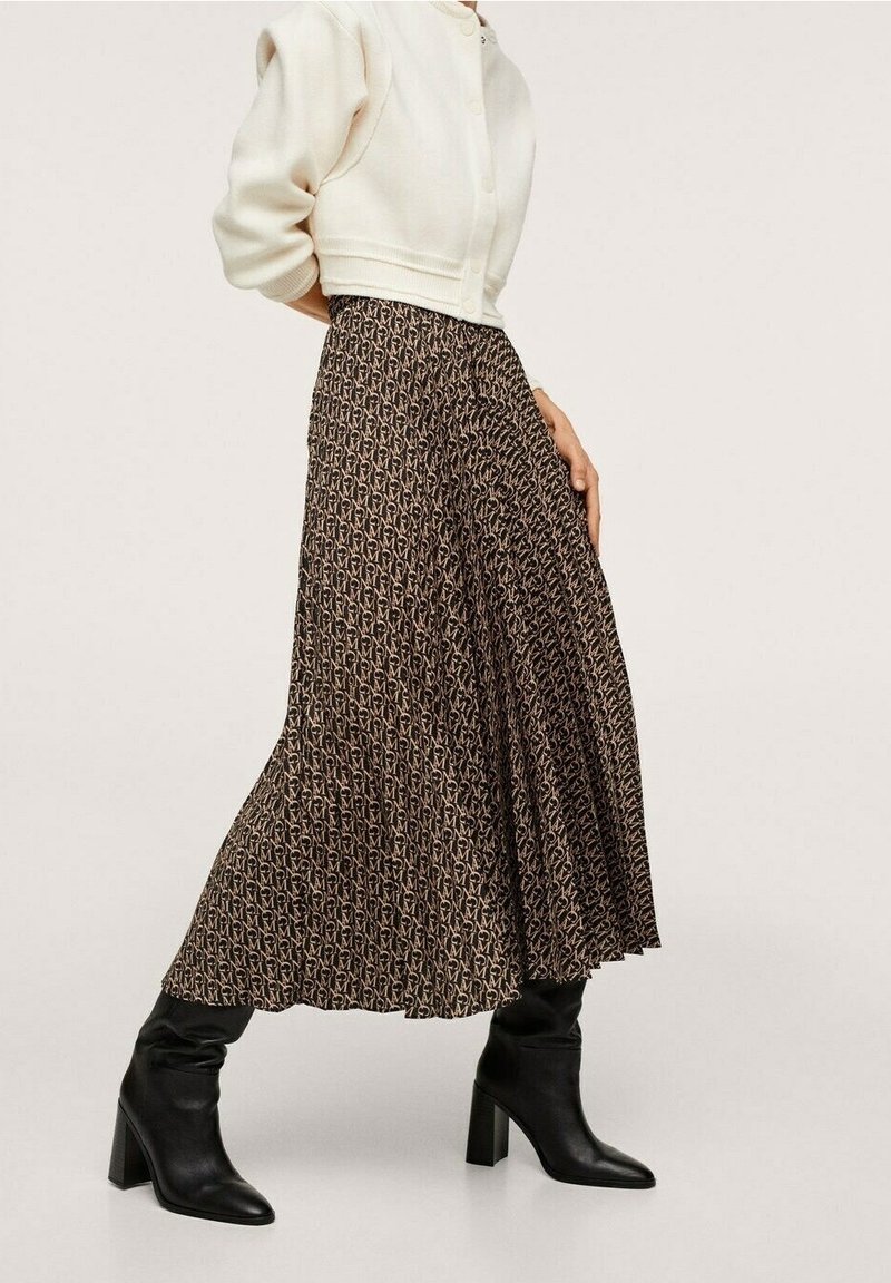 Jupe longue marron à motifs avec des plis, fabriquée en tissu léger. Présente un design fluide et se marie avec des bottes à talons noires.
