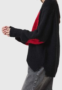 Czarny i czerwony dziane sweter o luźnym kroju, z ribbowanymi mankietami i asymetrycznym dołem. Tekstura wydaje się miękka i puszysta.