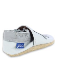 Witte leren schoen met grijze accenten, zachte textuur, ronde neus en klittenbandsluiting. Heeft een beige rubberen zool en een blauw logo-op-patch aan de zijkant.