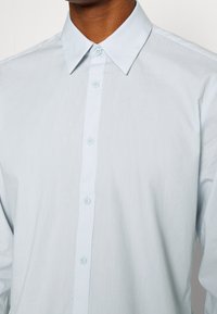Hellblaues Hemd mit klassischem Kragen, aus einem glatten Stoff, mit einer Knopfleiste vorne und fünf passenden Knöpfen.